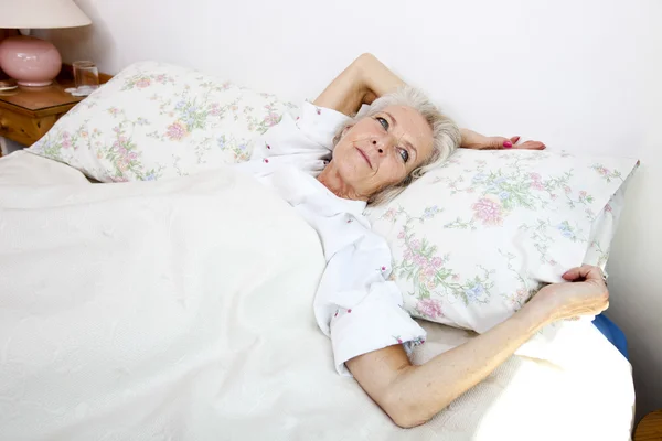Старшая женщина смотрит в сторону, лежа в постели — стоковое фото