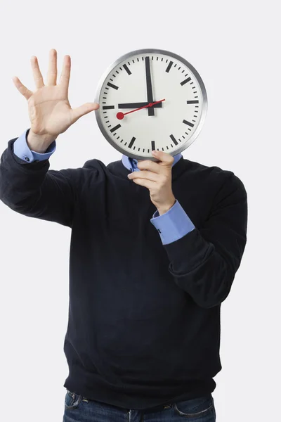 Человек держит часы над лицом — стоковое фото