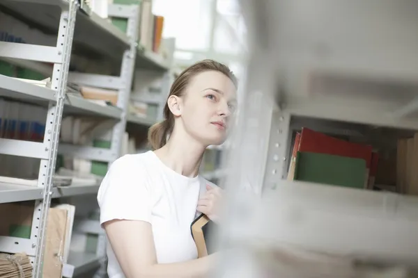 Young woman stands at library shelving — Stock Photo, Image