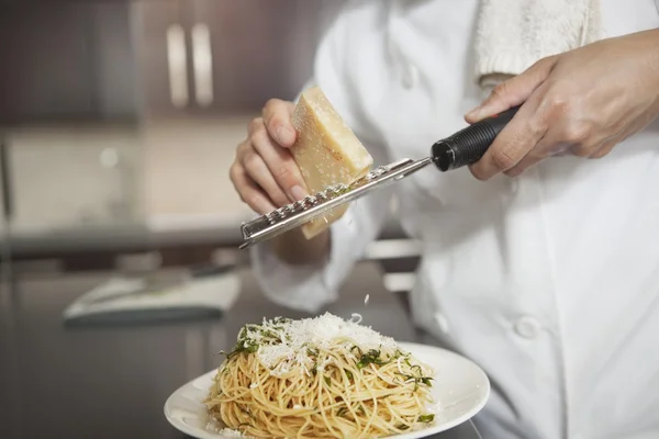 chef grating parmesan onto spaghetti