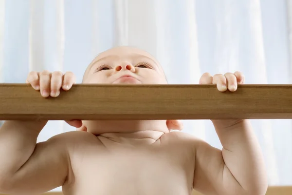 Infant child holding himself up in wooden cot — Stock Photo, Image