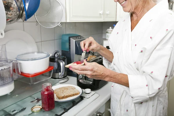 Äldre kvinna tillämpa sylt på toast — Stockfoto