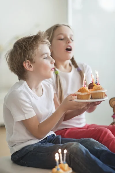 Siblings blowing candles on cupcakes — Stock Photo, Image
