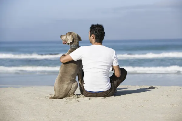 Człowiek i pies siedzi plaży — Zdjęcie stockowe