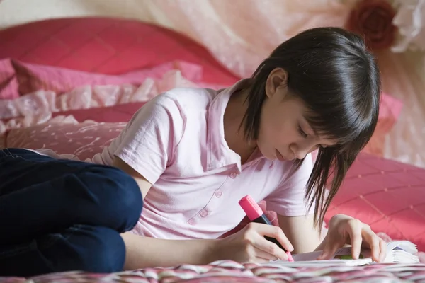 Teenage girl lying on bed doing homework — Stock Photo, Image