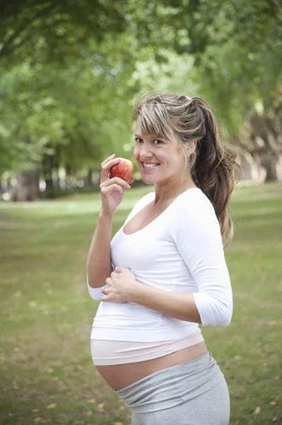 Беременная женщина в парке ест яблоко — стоковое фото