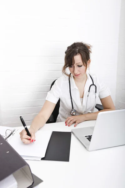 Arzt mit Laptop schreibt Notizen — Stockfoto