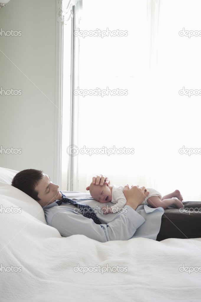 Working father lies with two week newborn on bed