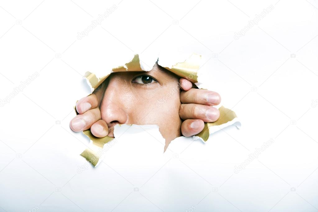 Man looking through ripped paper hole