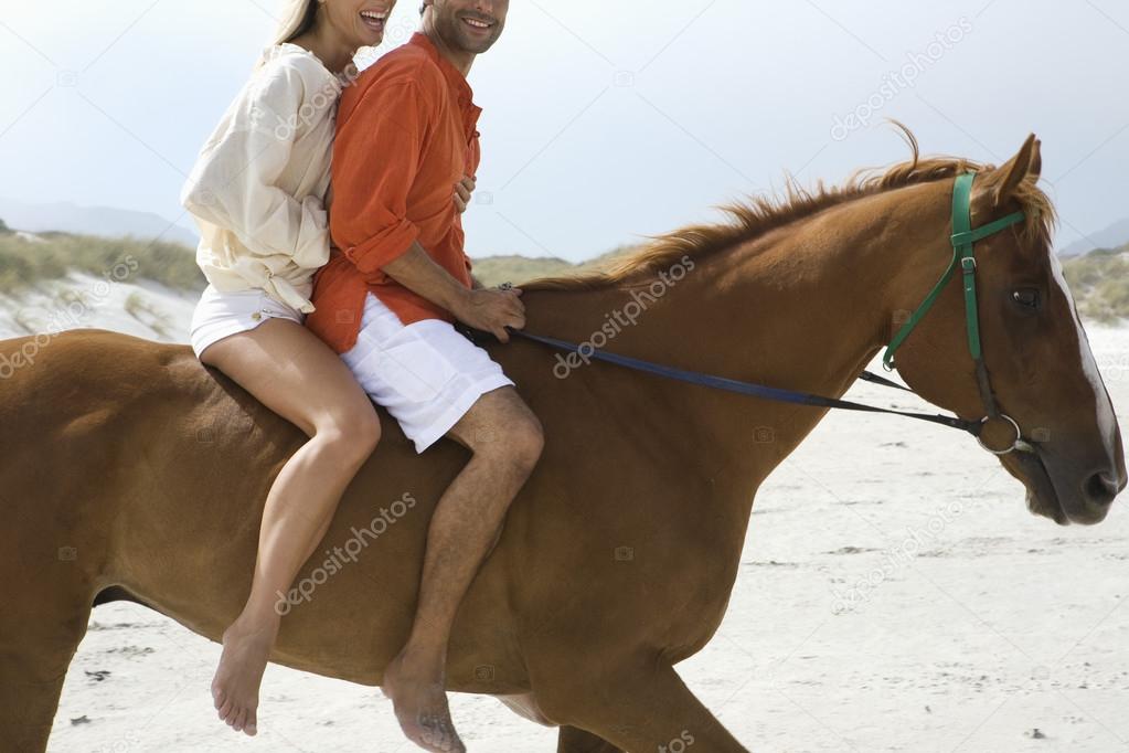 Couple riding horse on beach