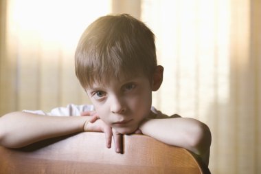 Çocuk sandalye sırtına yaslanmış kamera bakarak oturur