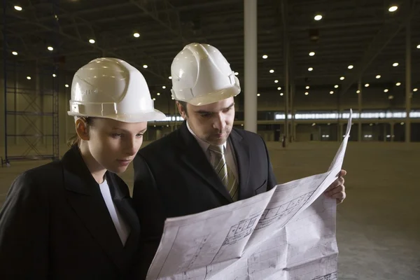 Colleagues study blueprint in empty warehouse — Stock Photo, Image