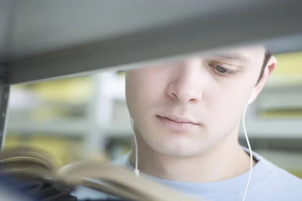 Joven leyendo en vista de biblioteca a través de estante —  Fotos de Stock