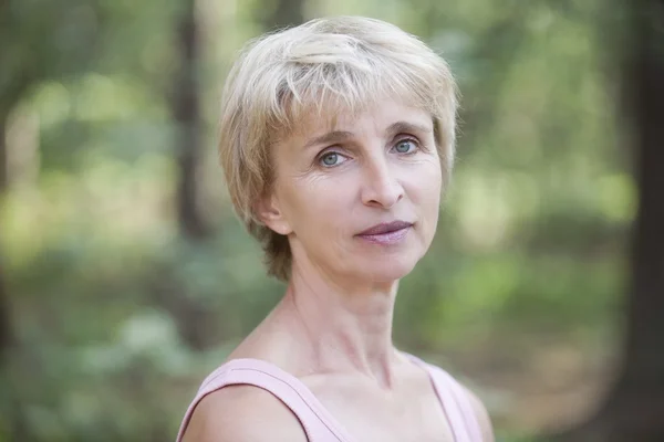 Mature woman stands in forest looking at camera — Stock Photo, Image