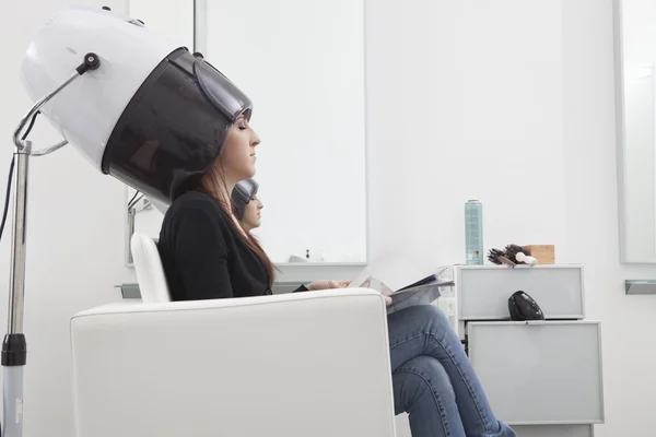 Female client sits under drying hood in hair salon — Stock Photo, Image