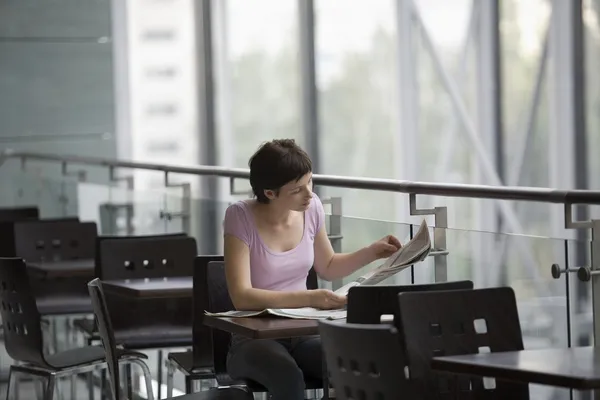 Mujer joven se sienta leyendo el periódico en la sala de comida del centro comercial — Foto de Stock