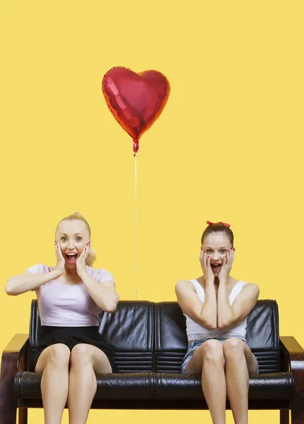 Verblüffte junge Frauen auf Sofa mit Ballon — Stockfoto