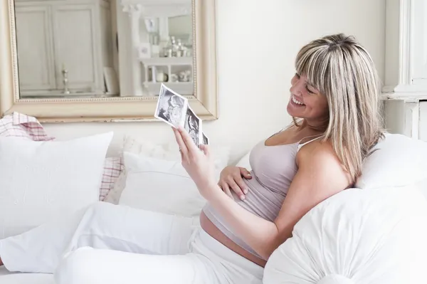 Femme enceinte assise sur un canapé avec des photos de bébé scan — Photo