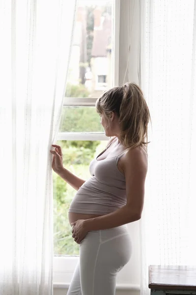 Femme enceinte regardant par la fenêtre — Photo