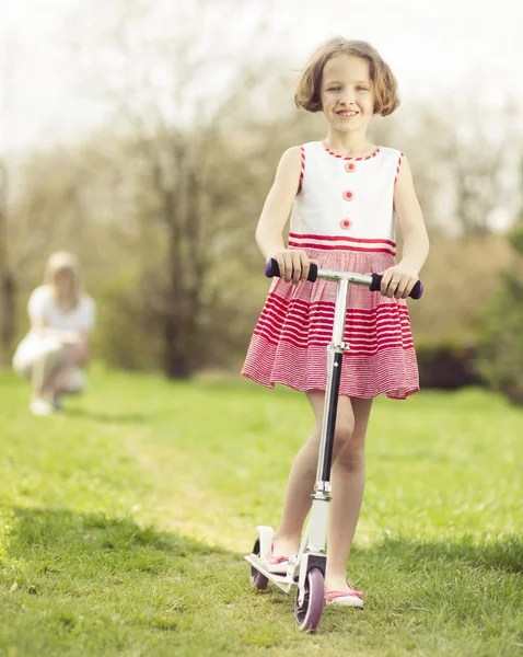 Meisje paardrijden scooter door park — Stockfoto