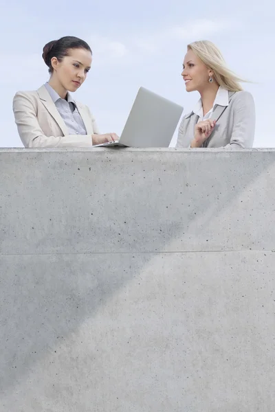 Femme d'affaires utilisant un ordinateur portable tout en étant debout avec un collègue — Photo