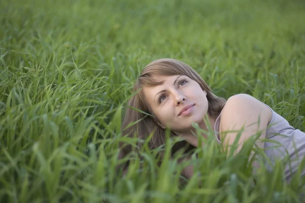 Junge Frau liegt in einem Grasfeld und schaut auf — Stockfoto