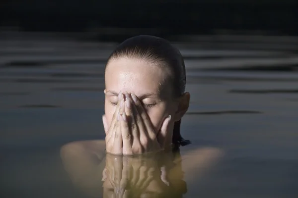 Jonge vrouw heeft betrekking op haar gezicht met haar handen in water — Stockfoto