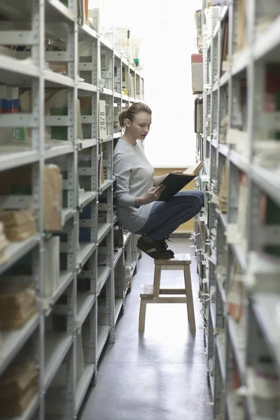 Woman crouches on stool in library — Stock Photo, Image