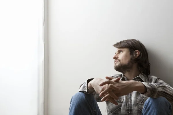 Jonge man in ingecheckte shirt zit met handen geklemd — Stockfoto