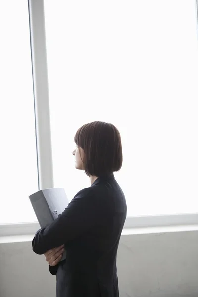 Γυναίκα των επιχειρήσεων που στέκεται με το αρχείο που ψάχνεις έξω από το παράθυρο — Φωτογραφία Αρχείου