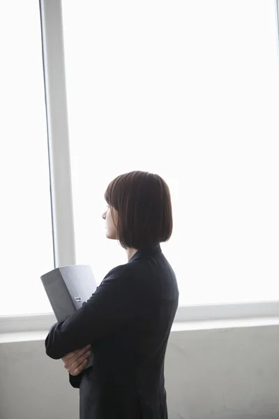 Zakenvrouw staat met bestand kijken uit venster — Stockfoto