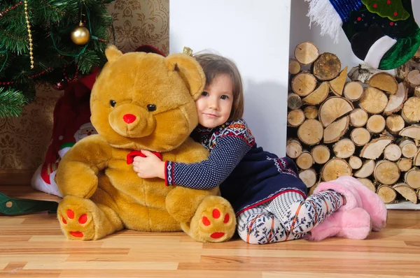 Cute dziewczynka przytulanie ogromny niedźwiedź w pobliżu choinki i kominkiem Zdjęcie Stockowe