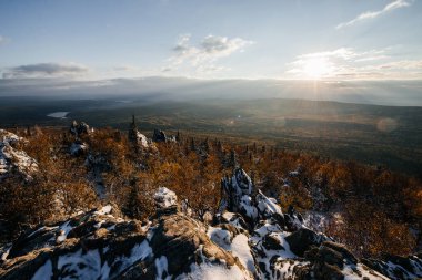 Dağın tepesinde gün batımı ve karla kaplı sarı sonbahar ormanı manzarası.