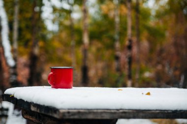 a red mug with coffee or tea is on a snow-covered table clipart