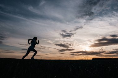Bir tarlada gün batımına karşı koşan bir kızın silueti.