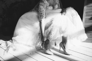 Beyaz elbiseli bir gelin elleriyle beyaz ayakkabılarını giyer.