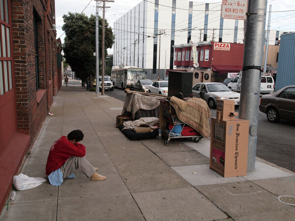 Homeless man sits on sidewalk with shopping carts full of his st