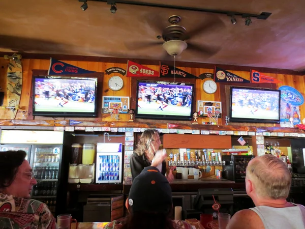 Ludzi siedzi w barze oglądać Liga gra powyżej barmana w ic — Zdjęcie stockowe