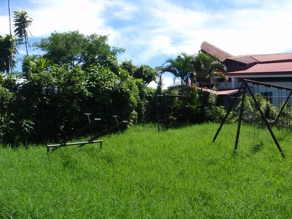 Balançoires rouillées, gymnase de jungle, et voir-scie dans l'herbe envahie — Photo