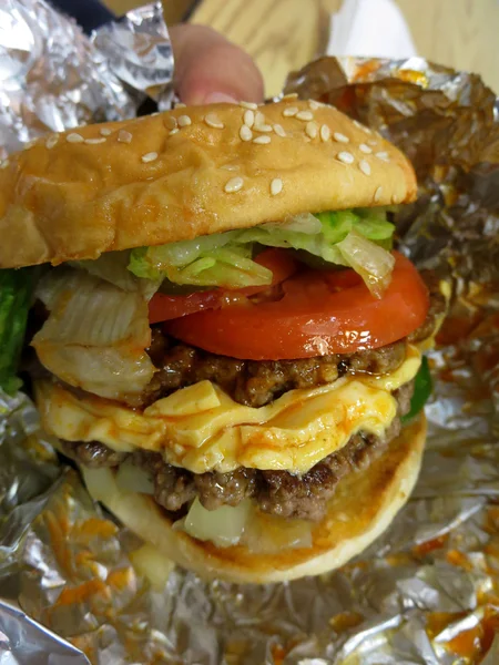 Close up van handen met hamburger verpakt in zilverpapier — Stockfoto