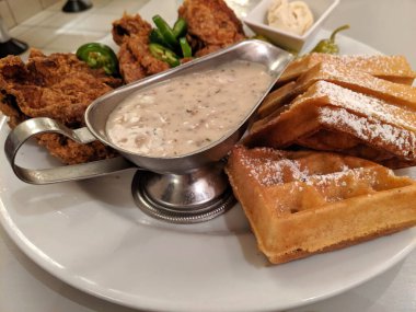 Yanında sos, tereyağı ve jalapeno dilimi olan beyaz tabakta tavuk ve waffle. Tavuk ve waffle, tavukla waffle 'ı birleştiren bir Amerikan yemeğidir. Ruh yiyeceği ve Pennsylvania Hollandalısı da dahil olmak üzere çeşitli aşçılık geleneklerinin bir parçasıdır.