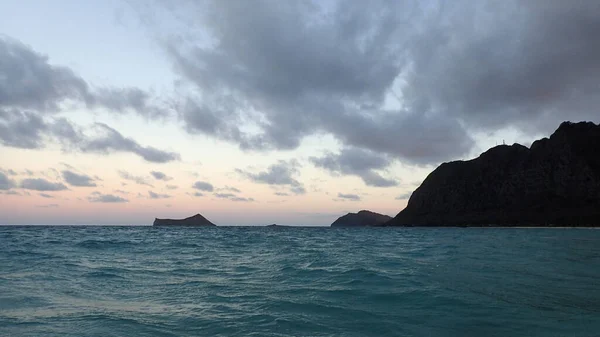 Gentle blue wave in Waimanalo Bay looking towards Rabbit island and Rock island at dusk on nice day Oahu, Hawaii.