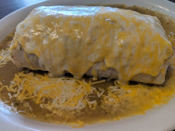 Wet Burrito with Green Sauce and melted cheese on top ala crate on Plate on table.