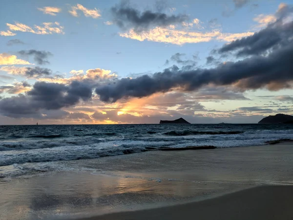 Sunrise over the ocean through the clouds on Waimanalo Beach with Rabbit and Rock Island in the distance on Oahu, Hawaii.