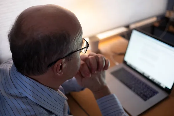 Senior man som arbetar med bärbar dator hemma och tänker på dokument. — Stockfoto