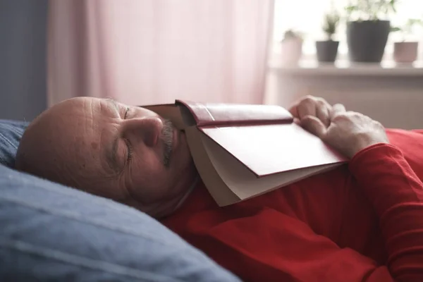Senior caucasian man sleeping with book on sofa napping — Stockfoto