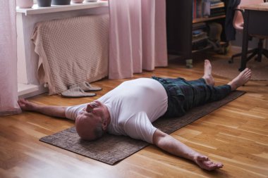 Kıdemli adam ahşap bir zeminde meditasyon yapıyor ve Shavasana pozunda yatıyor..