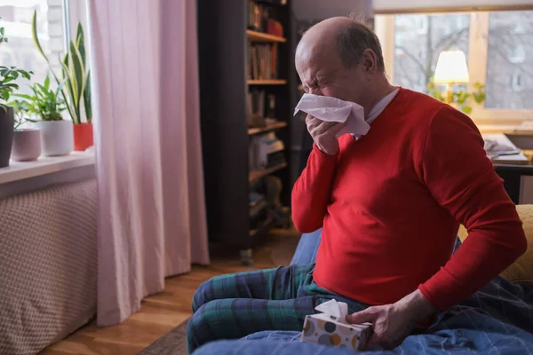 Senior man som håller en vävnad och nyser sitter hemma — Stockfoto