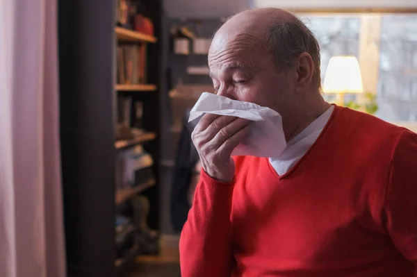 Senior man som håller en vävnad och nyser sitter hemma — Stockfoto