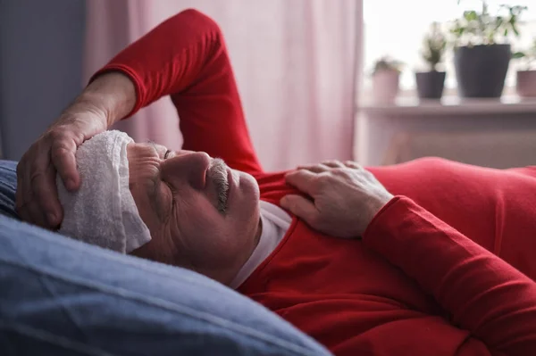 Un hombre enfermo durmiendo con una toalla húmeda en la frente para reducir la fiebre alta —  Fotos de Stock